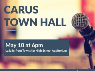 Microphone close-up on stage with text: "Carus Town Hall, May 10 at 6pm, LaSalle-Peru Township High School Auditorium." Logo at the bottom right corner.