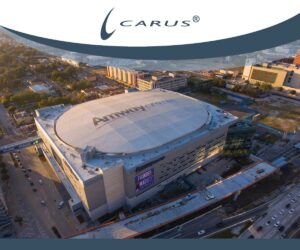 Aerial view of the Amway Center, a large arena with a round roof. Surrounding roads and buildings are visible. The arena has a white roof with the Amway Center logo. The scene is bathed in warm, golden light, indicating late afternoon or early evening.