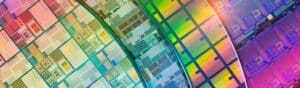 Close-up image of colorful semiconductor wafers with intricate patterns and circuits. The wafers display a spectrum of colors due to light reflection, showcasing the complex technology involved in microchip production.