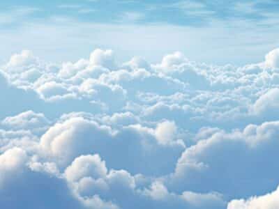 A panoramic view of a sky filled with fluffy, white clouds under a blue sky. Soft sunlight illuminates the clouds, creating a serene and peaceful atmosphere.