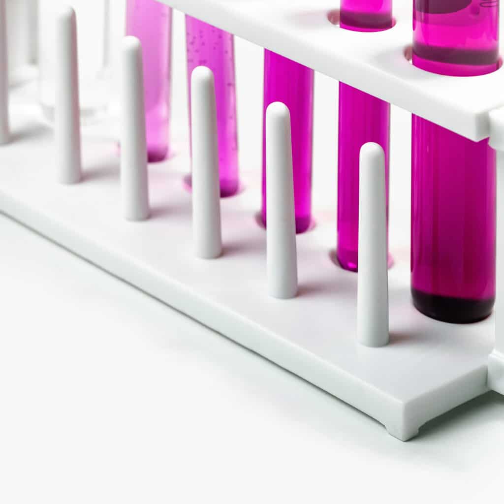 Test tubes filled with pink liquid are placed in a white plastic rack. The image focuses on the varying shades and levels of the liquid in the tubes, emphasizing a clean and organized laboratory setting.