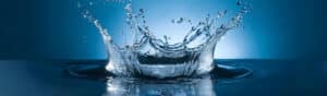 A close-up image of a water splash captured mid-air, forming intricate patterns against a blue gradient background. Ripples spread outward from the center, creating a sense of motion and fluidity.